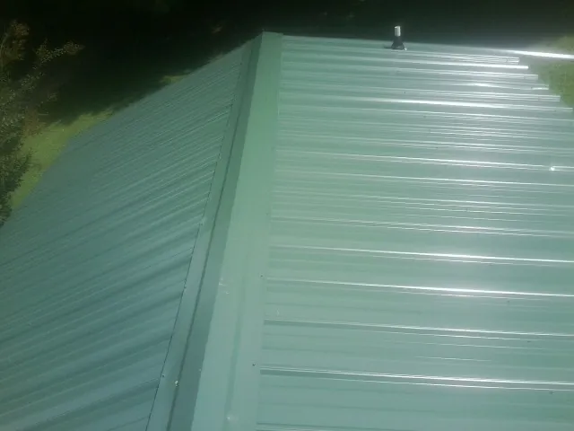 New green metal panels meeting at the ridge of a roof — Flat Roof Repair work by our crew in Andover